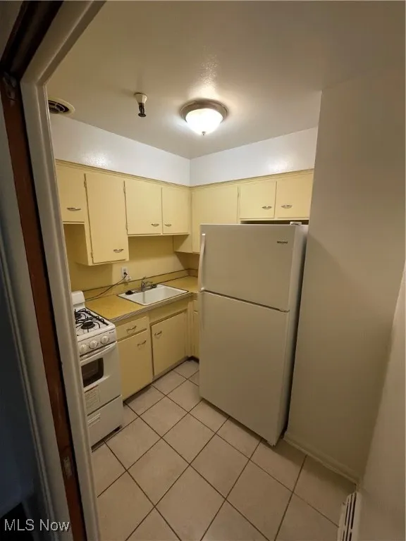 Kitchen with refrigerator, stove, a sink, light countertops, and light tile patterned floors