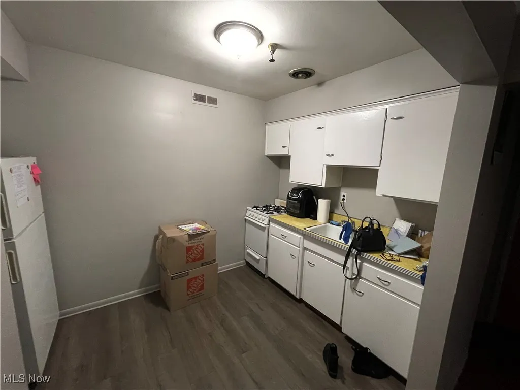 Kitchen with white appliances, white cabinets, light countertops, dark wood-type flooring, and a sink