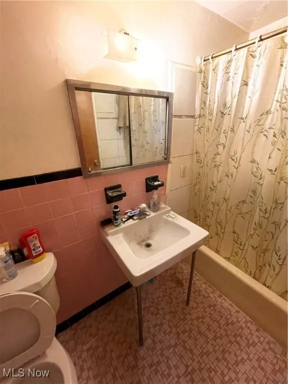 Full bathroom featuring tile walls, curtained shower, toilet, wainscoting, and tile patterned floors