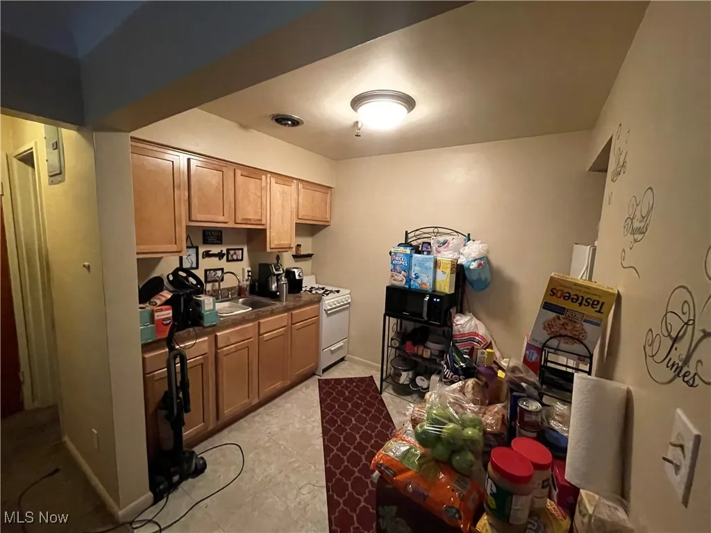 Kitchen featuring white range with gas cooktop, a sink, dark countertops, and baseboards