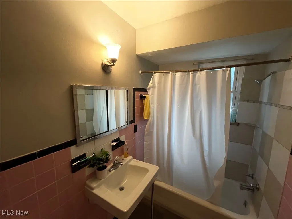 Full bathroom with tile walls, shower / bath combo, a sink, and wainscoting