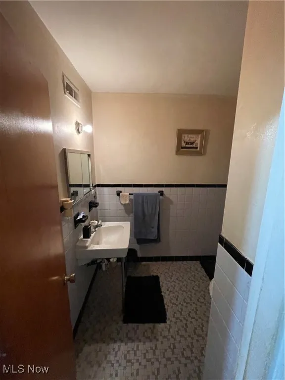Half bath with tile walls, a sink, and wainscoting