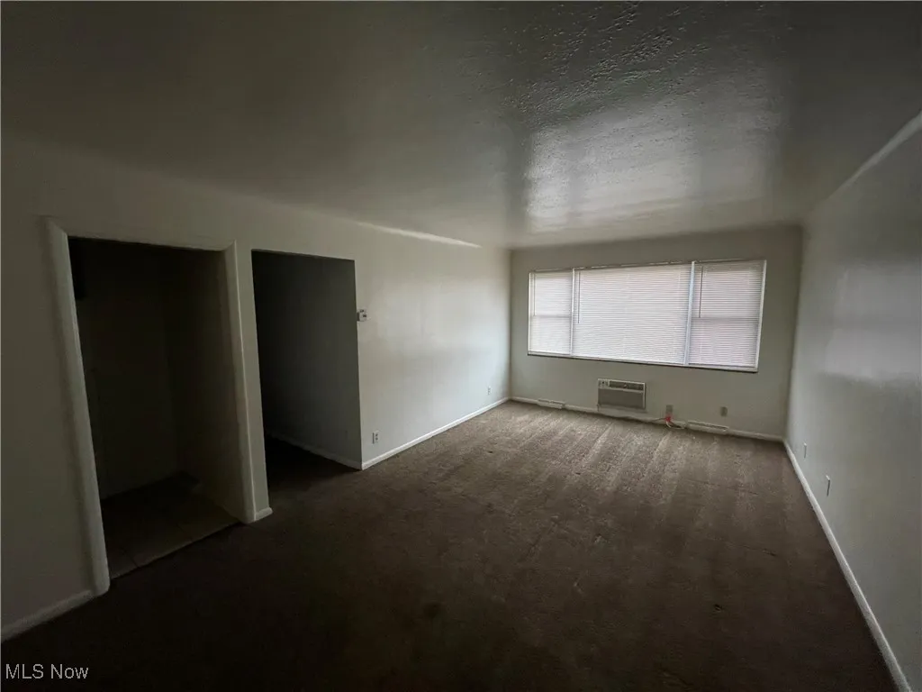 Unfurnished bedroom with a wall unit AC, dark colored carpet, baseboards, and a textured ceiling