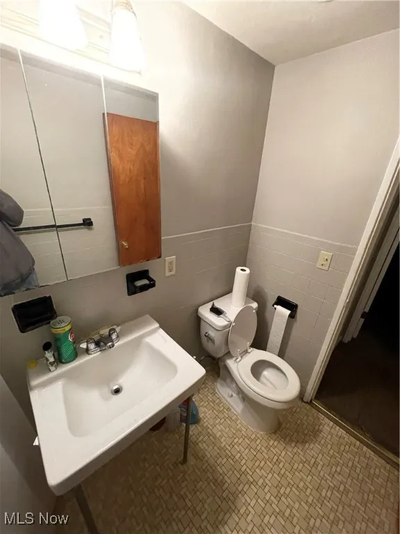 Bathroom featuring toilet, tile walls, and a sink
