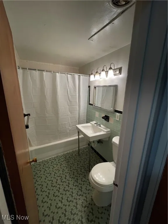 Full bathroom with toilet, tile patterned floors, shower / tub combo with curtain, and tile walls