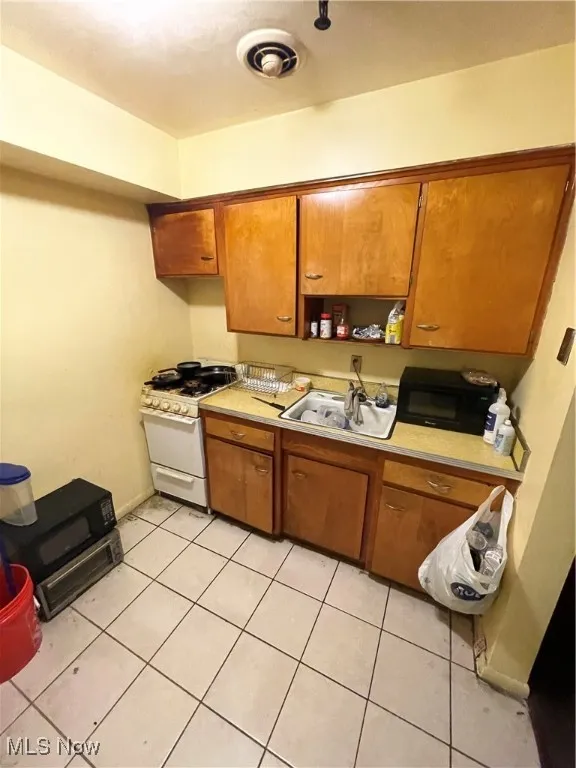 Kitchen featuring range, a sink, brown cabinetry, light tile patterned floors, and light countertops