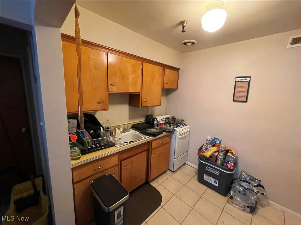 Kitchen featuring white gas stove, a sink, brown cabinets, light tile patterned floors, and light countertops
