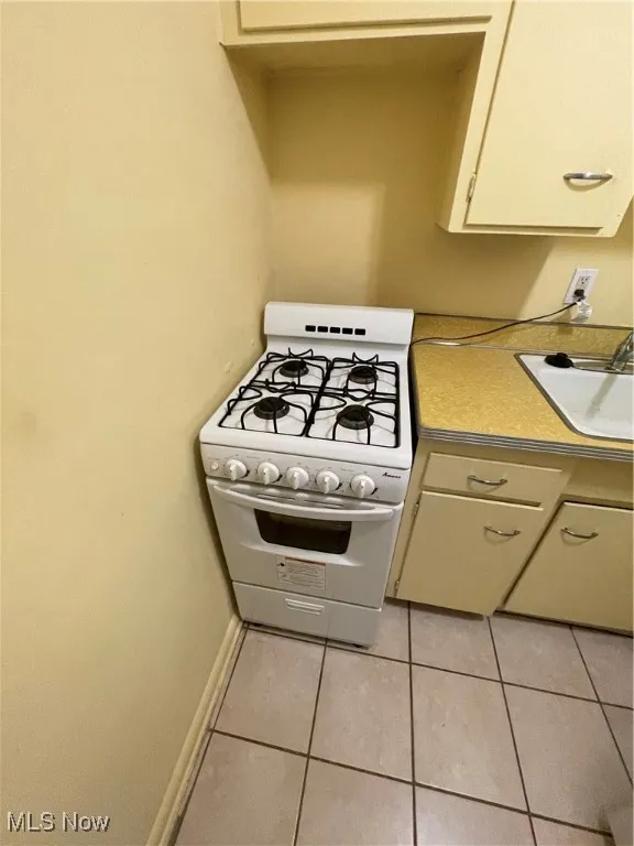 Kitchen with white gas stove, light tile patterned flooring, a sink, light countertops, and baseboards