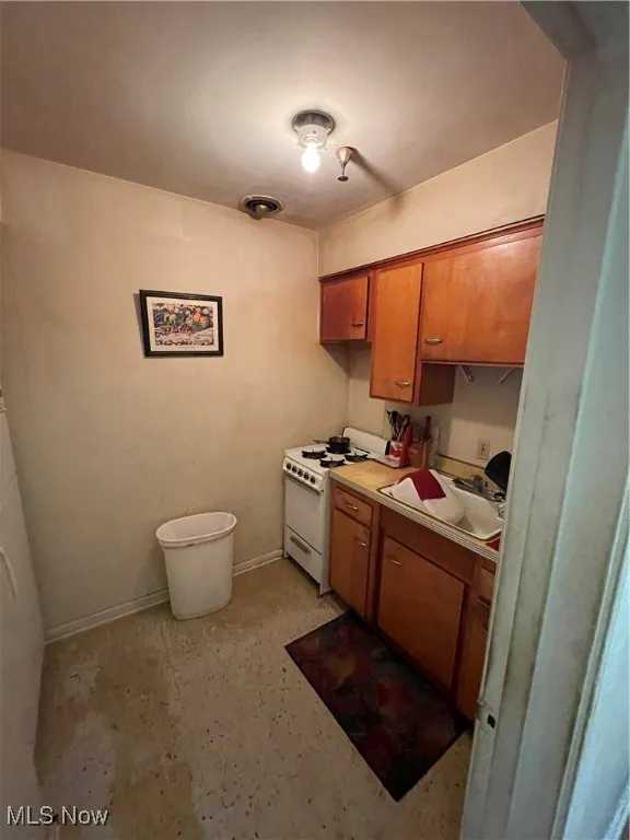 Kitchen featuring white gas range oven, a sink, brown cabinetry, light countertops, and baseboards