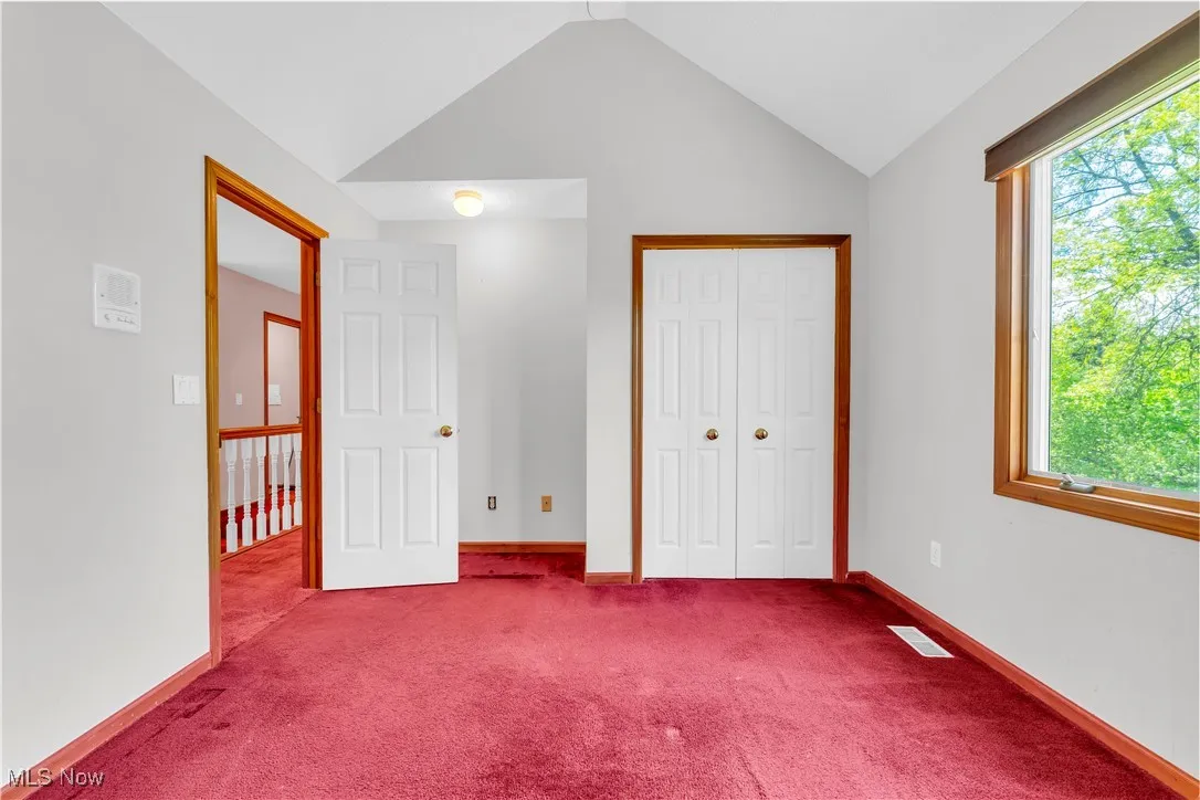Unfurnished bedroom with multiple windows, vaulted ceiling, carpet floors, a closet, and baseboards
