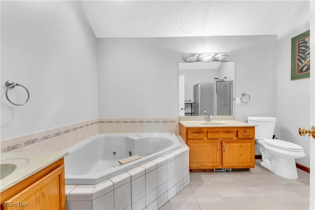 Full bathroom featuring a textured ceiling, a stall shower, vanity, a jetted tub, and toilet