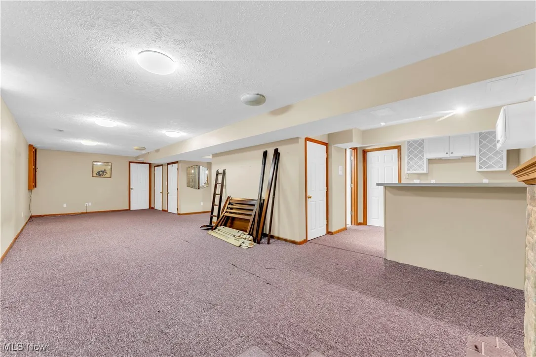 Finished basement featuring light colored carpet, a textured ceiling, baseboards, and bar