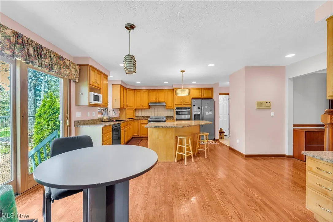 Kitchen with stainless steel appliances, a sink, light wood-style flooring, a center island, and backsplash