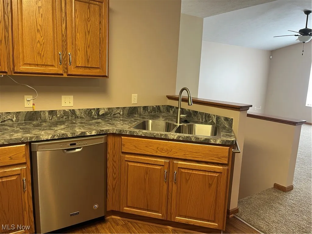 Kitchen with dishwasher, a sink, brown cabinets, and a ceiling fan