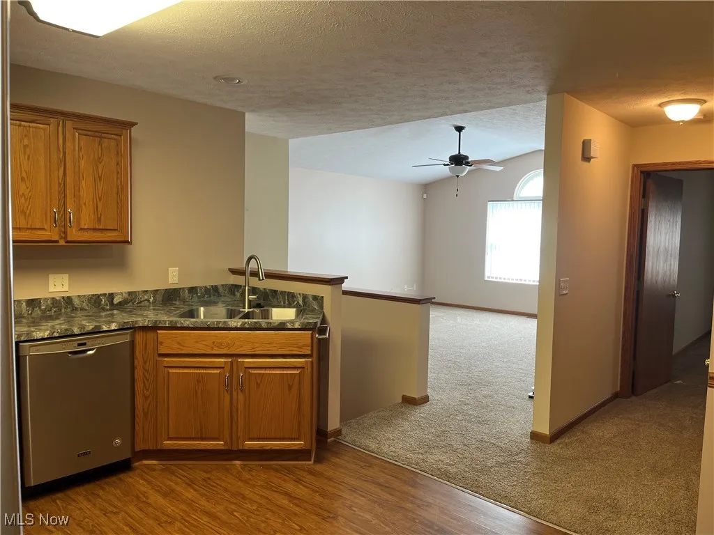 Kitchen featuring stainless steel dishwasher, a sink, a peninsula, brown cabinets, and a ceiling fan