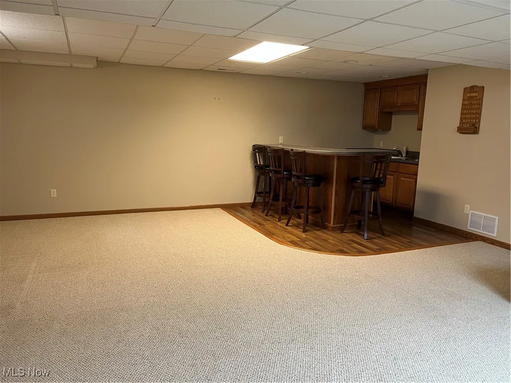 Indoor bar with dark colored carpet, baseboards, and a paneled ceiling