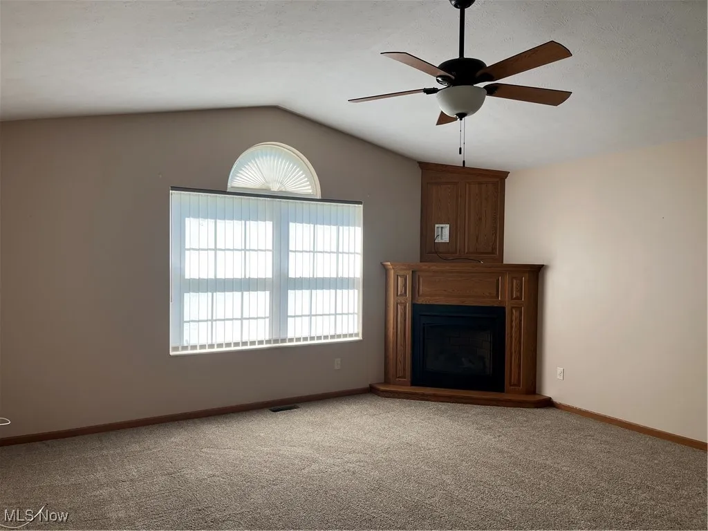 Unfurnished living room featuring a ceiling fan, lofted ceiling, healthy amount of natural light, carpet, and baseboards