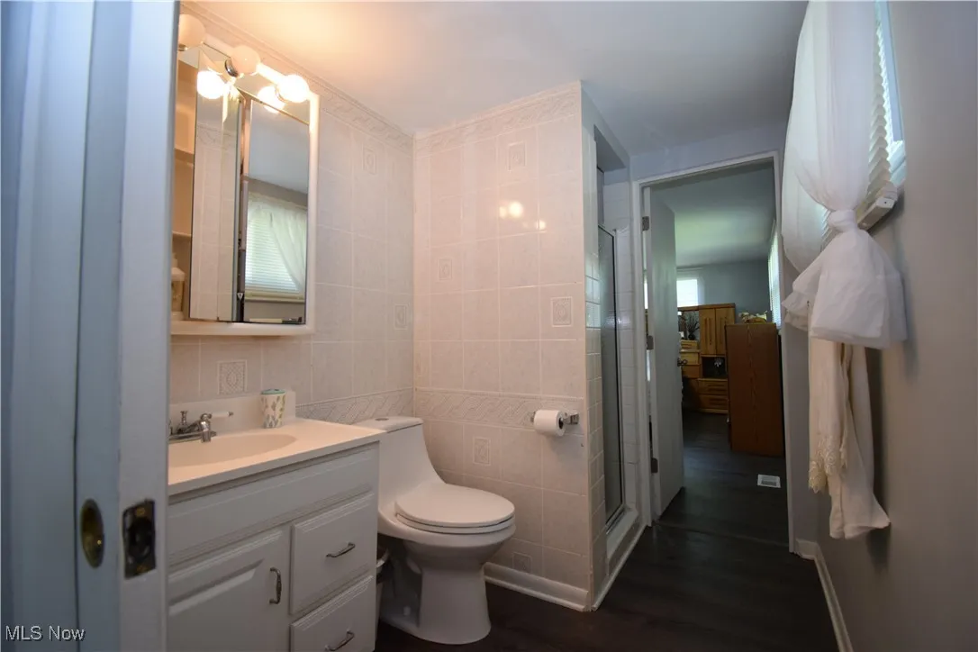 Bathroom featuring tile walls, vanity, wood finished floors, toilet, and a stall shower
