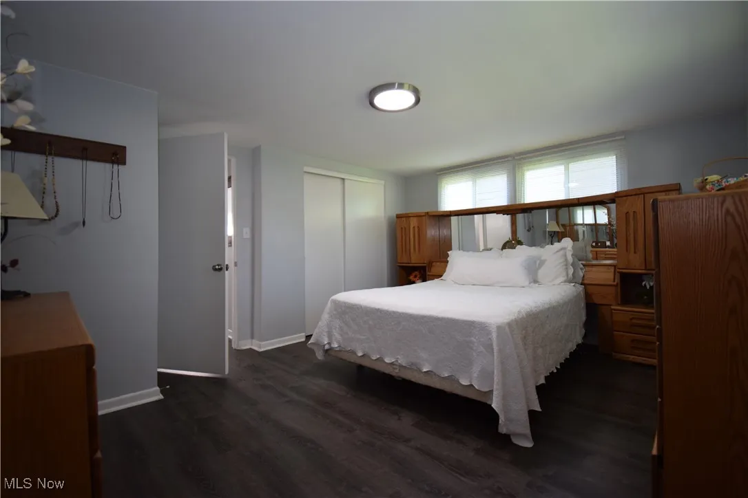 Bedroom with dark wood-style flooring, baseboards, and a closet