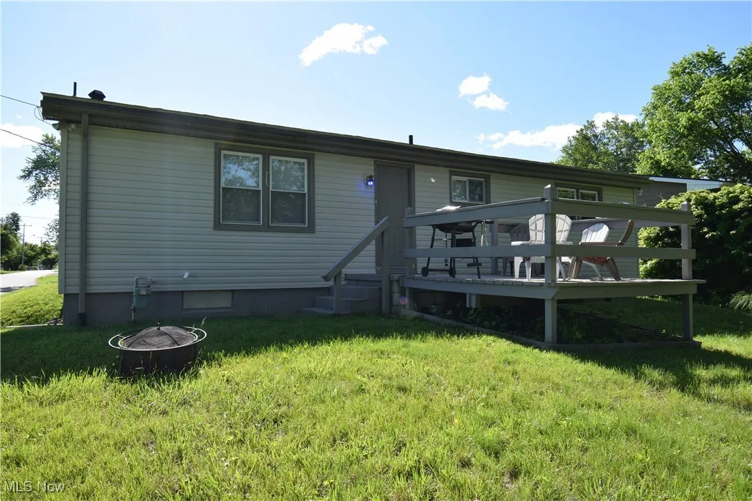 Rear view of house with a fire pit, a wooden deck, and a yard