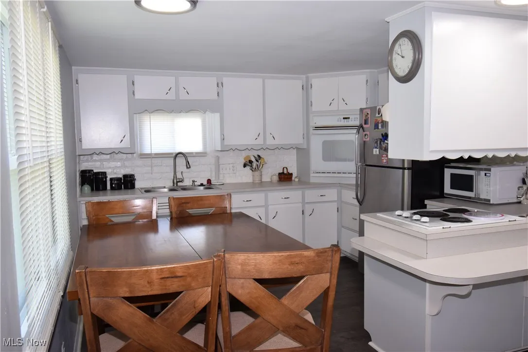 Kitchen with a sink, white appliances, light countertops, and white cabinets
