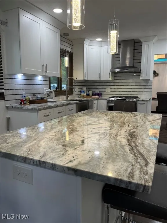 Kitchen with exhaust hood, decorative backsplash, range, light stone counters, and white cabinets