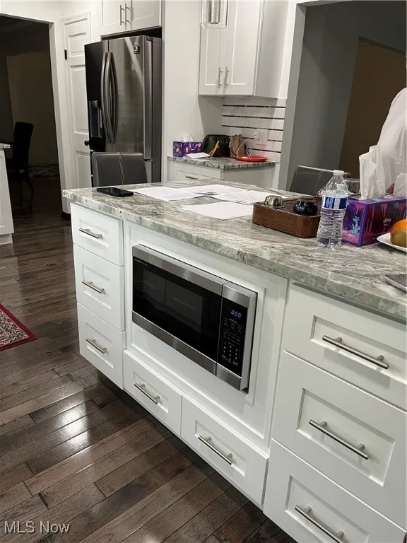 Kitchen with fridge, dark wood-type flooring, stainless steel microwave, and white cabinets