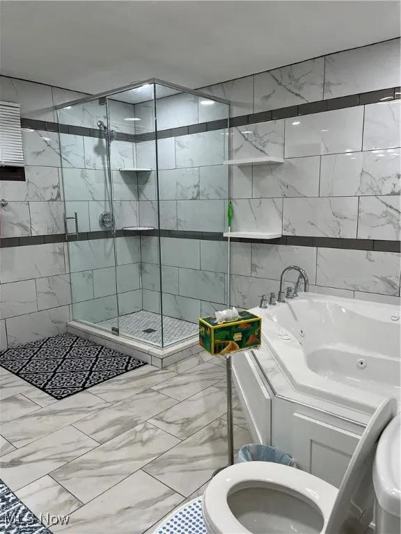 Full bathroom featuring marble look tile flooring, a stall shower, a jetted tub, tile walls, and toilet