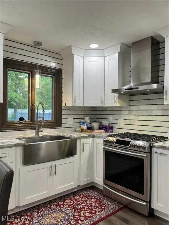 Kitchen featuring ventilation hood, range, a sink, white cabinets, and a textured ceiling