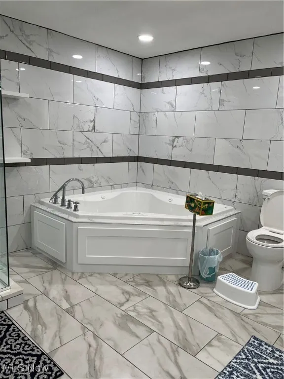 Bathroom with marble look tiles, tile walls, a garden tub, and toilet