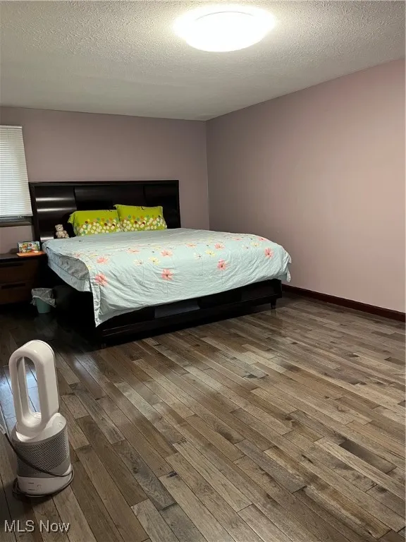 Bedroom featuring wood-type flooring, a textured ceiling, and baseboards