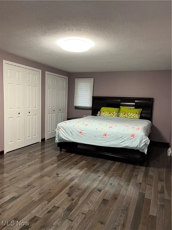 Bedroom with hardwood / wood-style floors, a textured ceiling, two closets, and baseboards