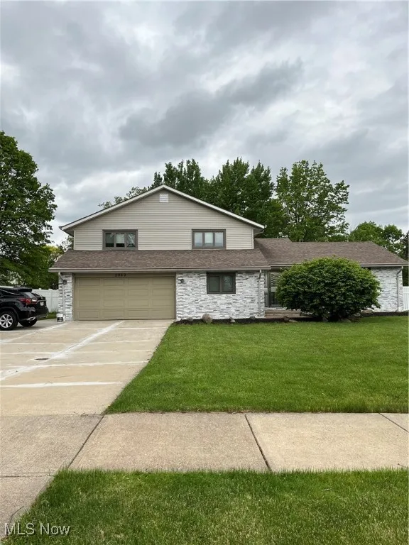 View of front facade with an attached garage, stone siding, driveway, a front yard, and roof with shingles
