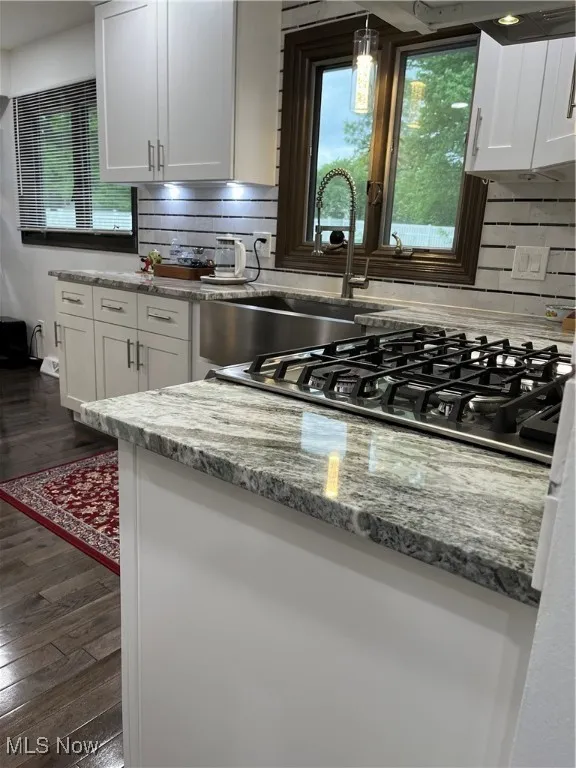 Kitchen with dark wood-style floors, white cabinetry, backsplash, and light stone counters