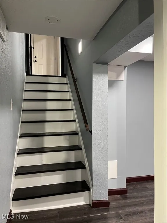 Staircase with wood finished floors, a textured wall, and baseboards
