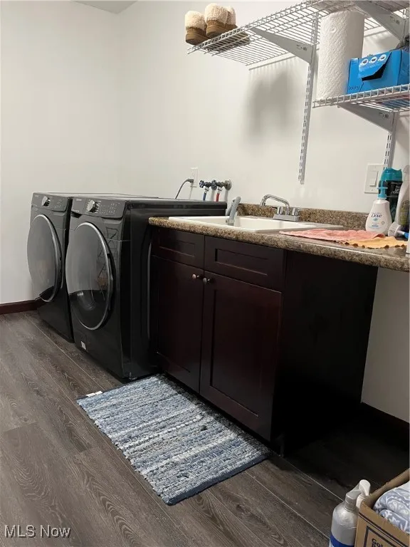 Washroom with washing machine and clothes dryer, dark wood-type flooring, cabinet space, and baseboards