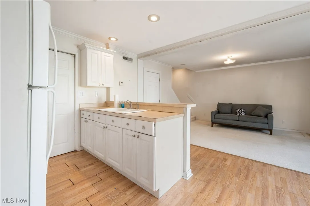 Kitchen featuring freestanding refrigerator, a sink, a peninsula, crown molding, and open floor plan
