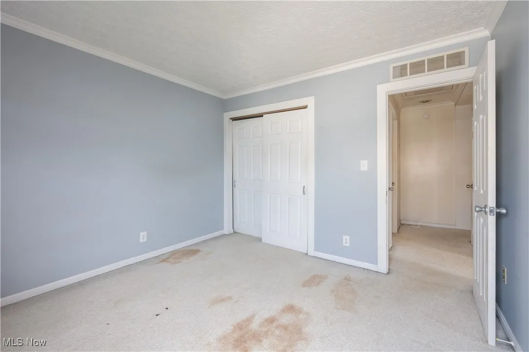 Unfurnished bedroom with a closet, carpet flooring, a textured ceiling, baseboards, and crown molding
