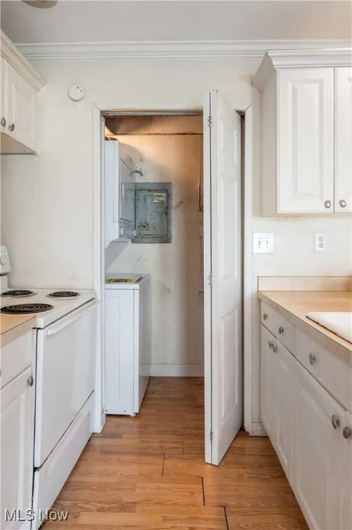 Kitchen with electric range, ornamental molding, laminate floors, light countertops, and white cabinetry