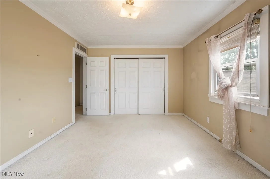 Unfurnished bedroom with light carpet, a closet, baseboards, crown molding, and a textured ceiling