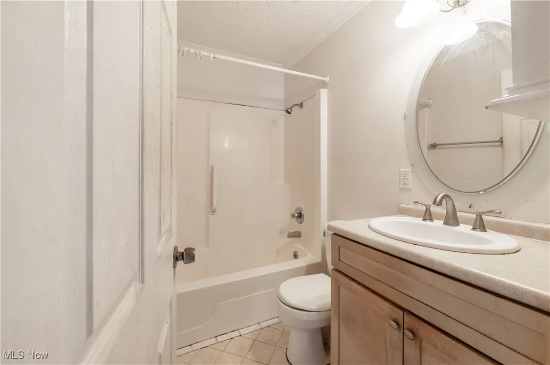 Full bathroom featuring a textured ceiling, tile patterned flooring, toilet, vanity, and  shower combination