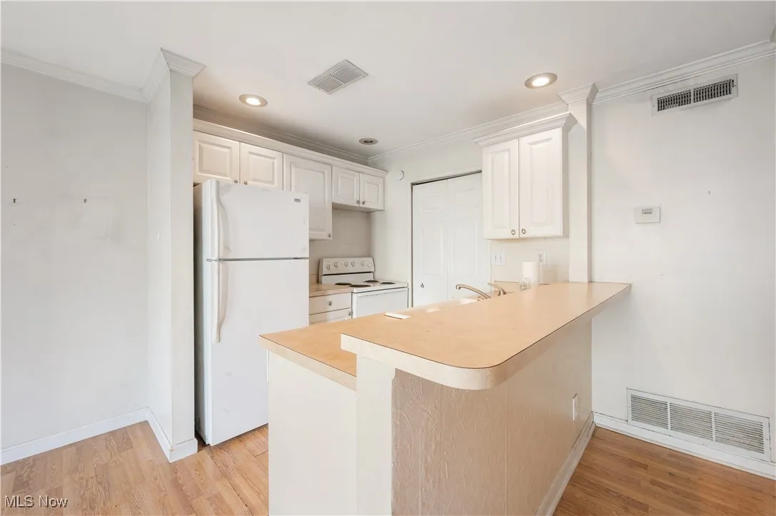 Kitchen featuring white appliances, ornamental molding, a peninsula, light countertops, and light laminate flooring