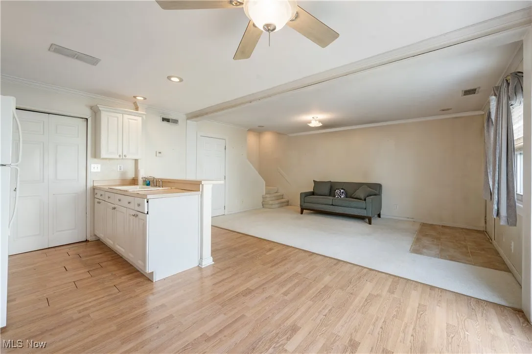 Kitchen featuring crown molding, light laminate finished floors, a sink, white cabinetry, and a peninsula