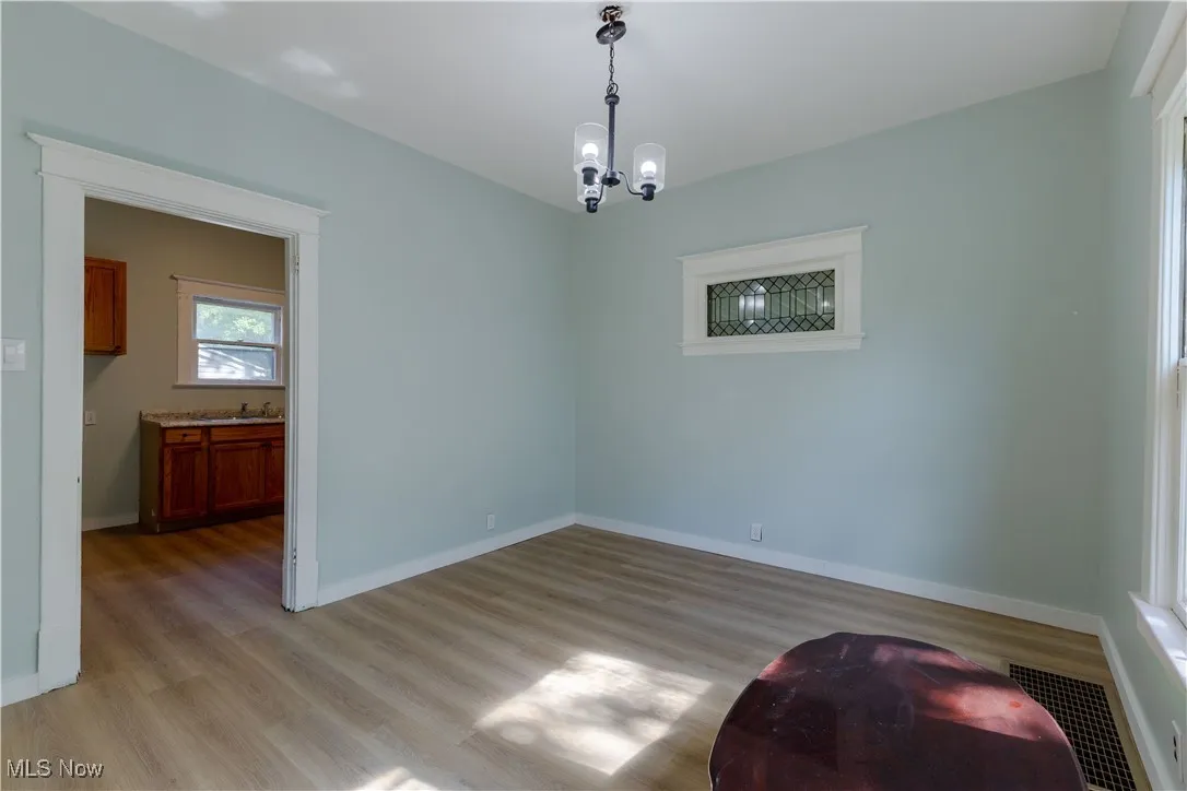 Unfurnished room featuring a chandelier, light wood-style floors, baseboards, and a sink