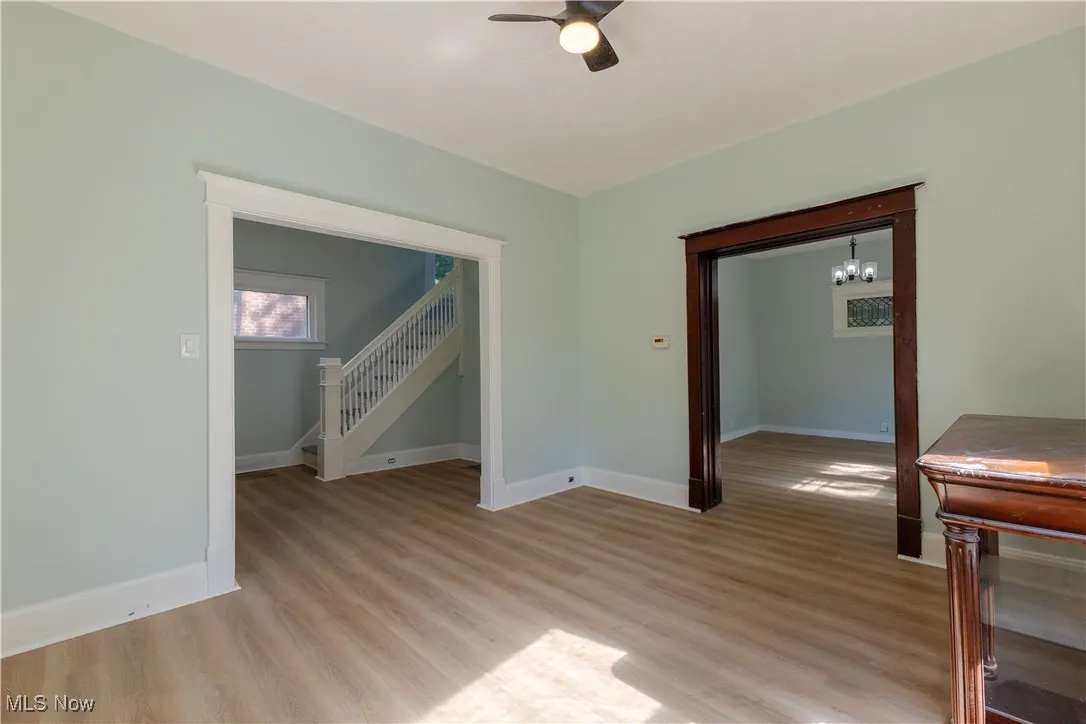 Spare room featuring ceiling fan, light wood finished floors, baseboards, and a chandelier