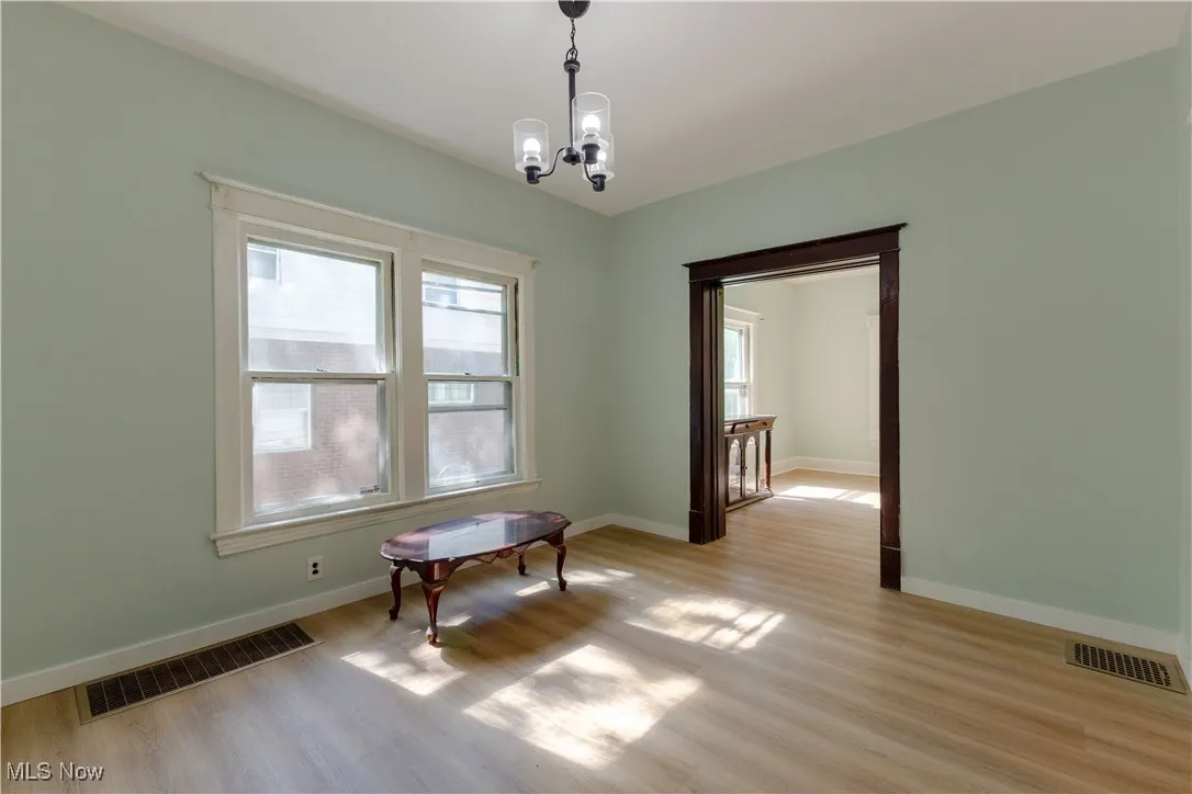 Unfurnished room featuring light wood finished floors, a chandelier, and baseboards