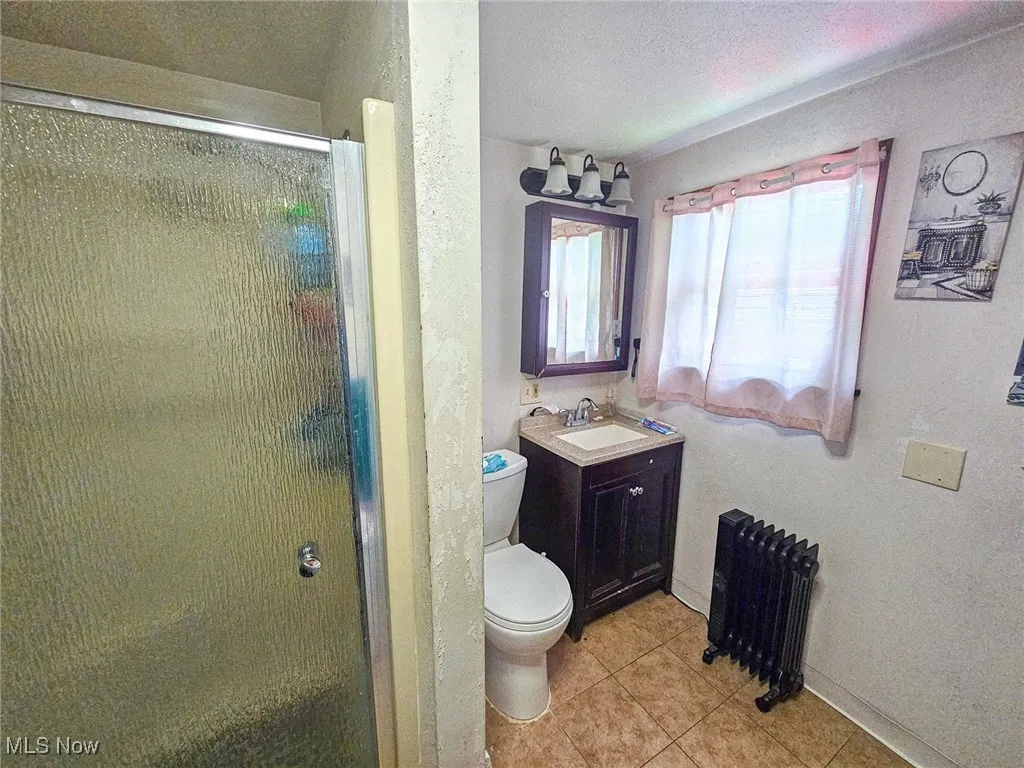 Bathroom featuring radiator heating unit, toilet, tile patterned floors, a stall shower, and a textured ceiling