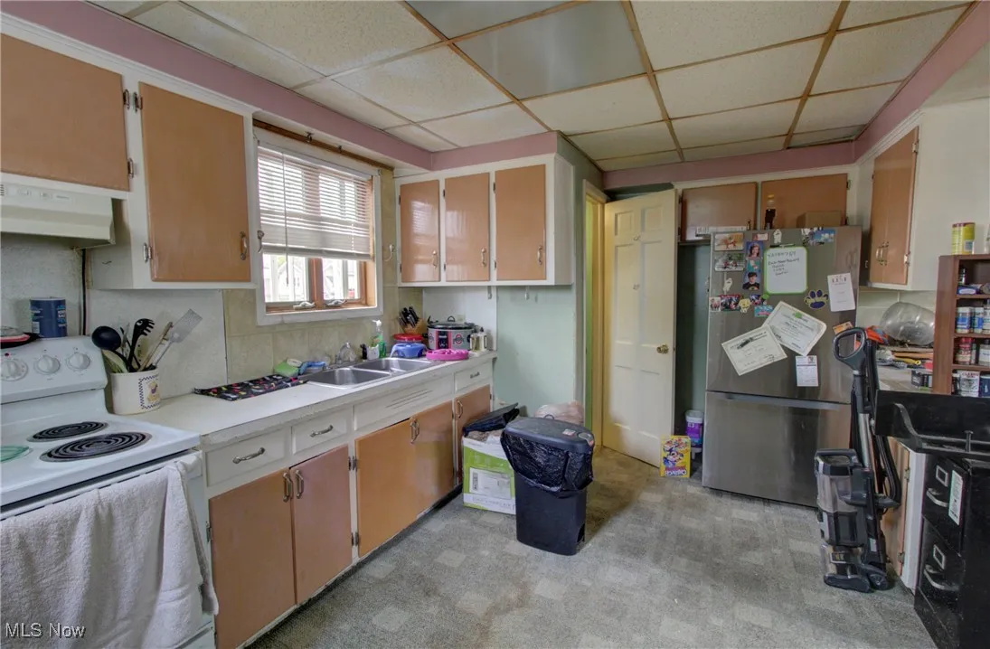 Kitchen featuring white electric range oven, freestanding refrigerator, range hood, a paneled ceiling, and light countertops