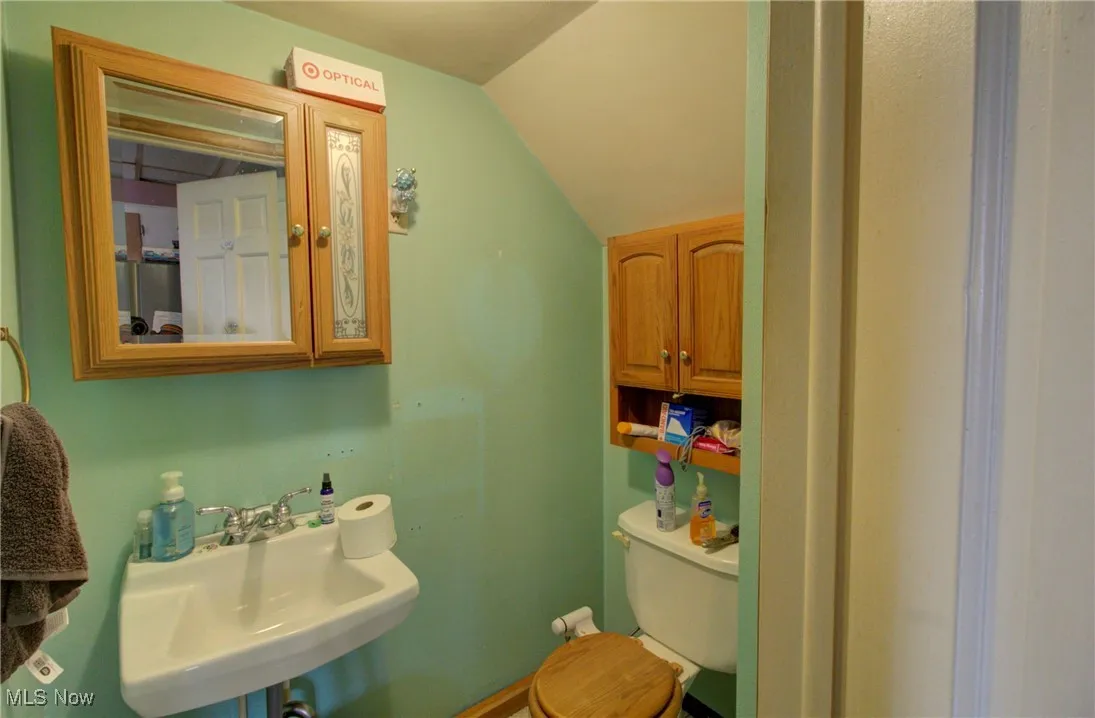 Half bathroom featuring a sink, toilet, and vaulted ceiling