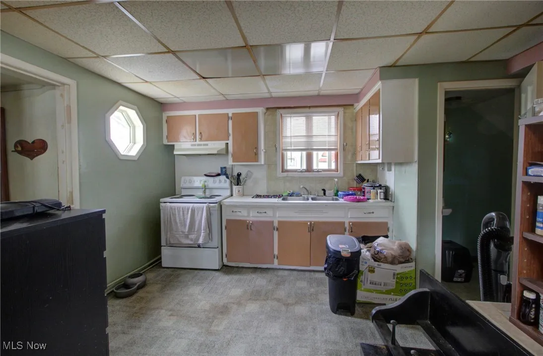 Kitchen with electric range, a drop ceiling, a sink, light countertops, and under cabinet range hood